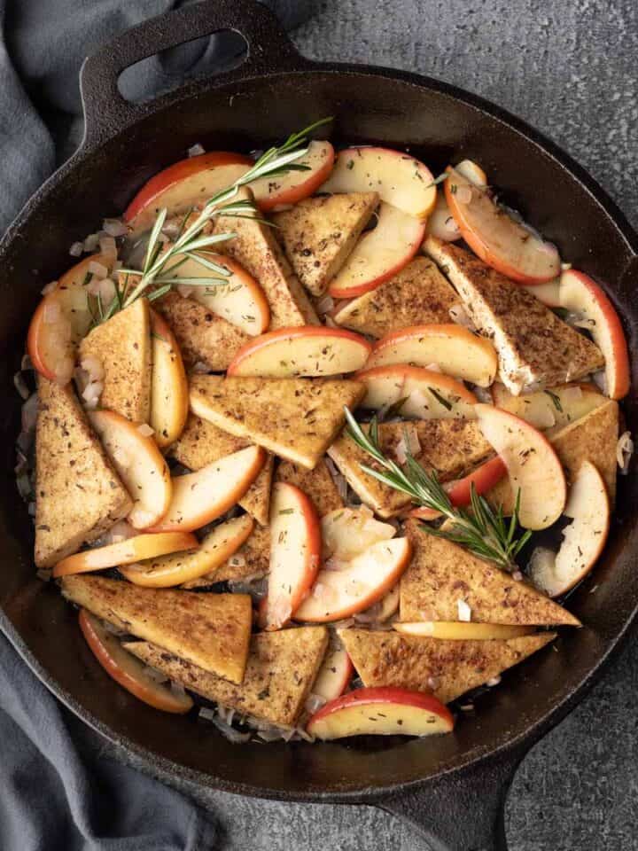 A large skillet filled with tofu, apples, rosemary, and shallot, and glazed with apple cider.