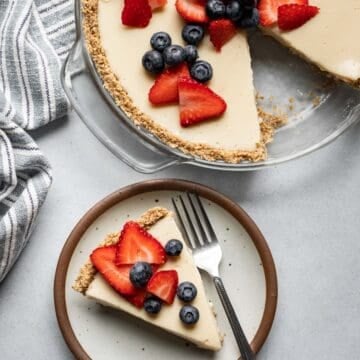 Whole tofu cheesecake topped with berries with one slice on a small plate.
