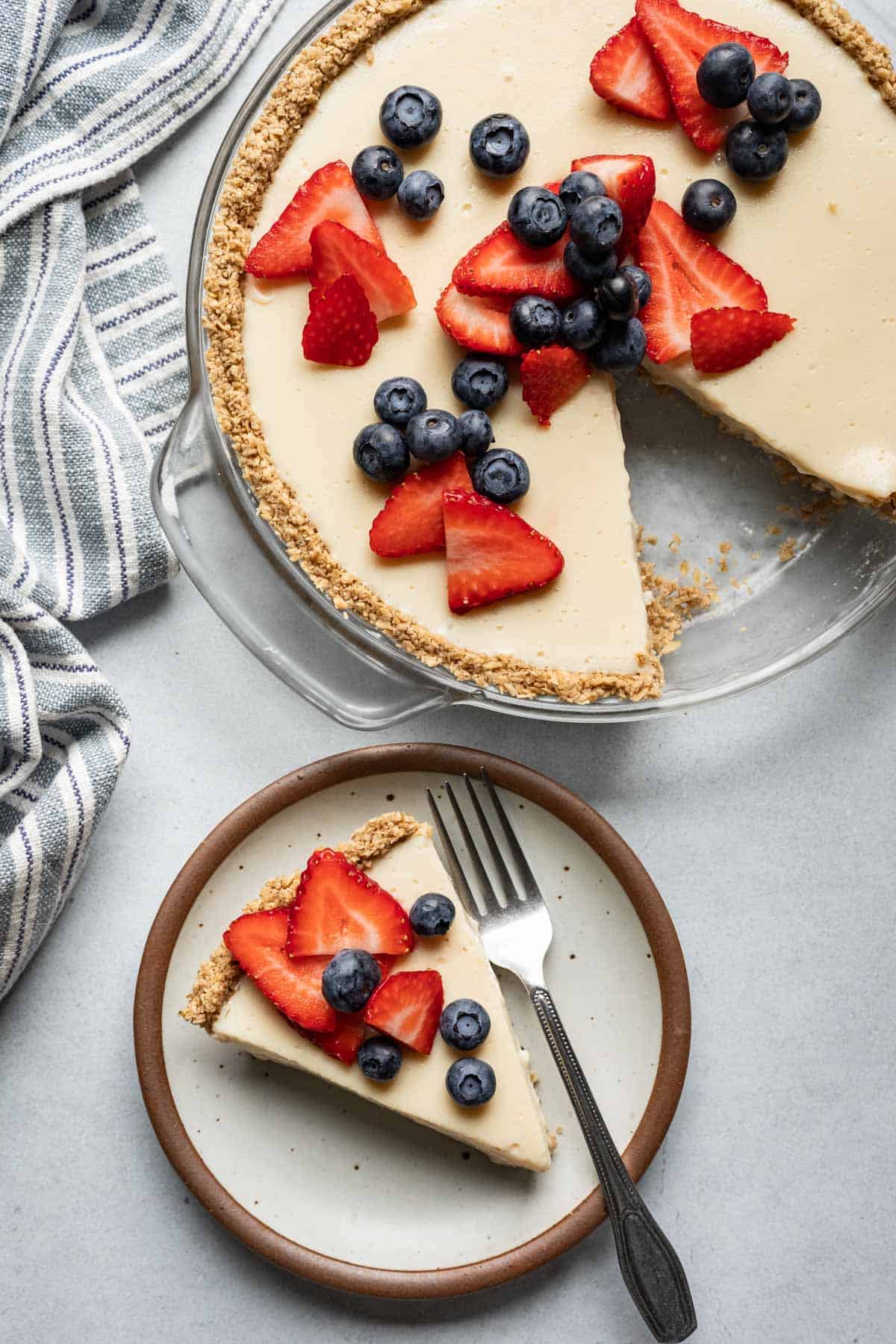 A tofu cheesecake topped with blueberries and strawberries with one slice on a plate.