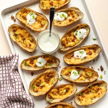 A large baking sheet filled with cheesy potato skins garnished with green onion.