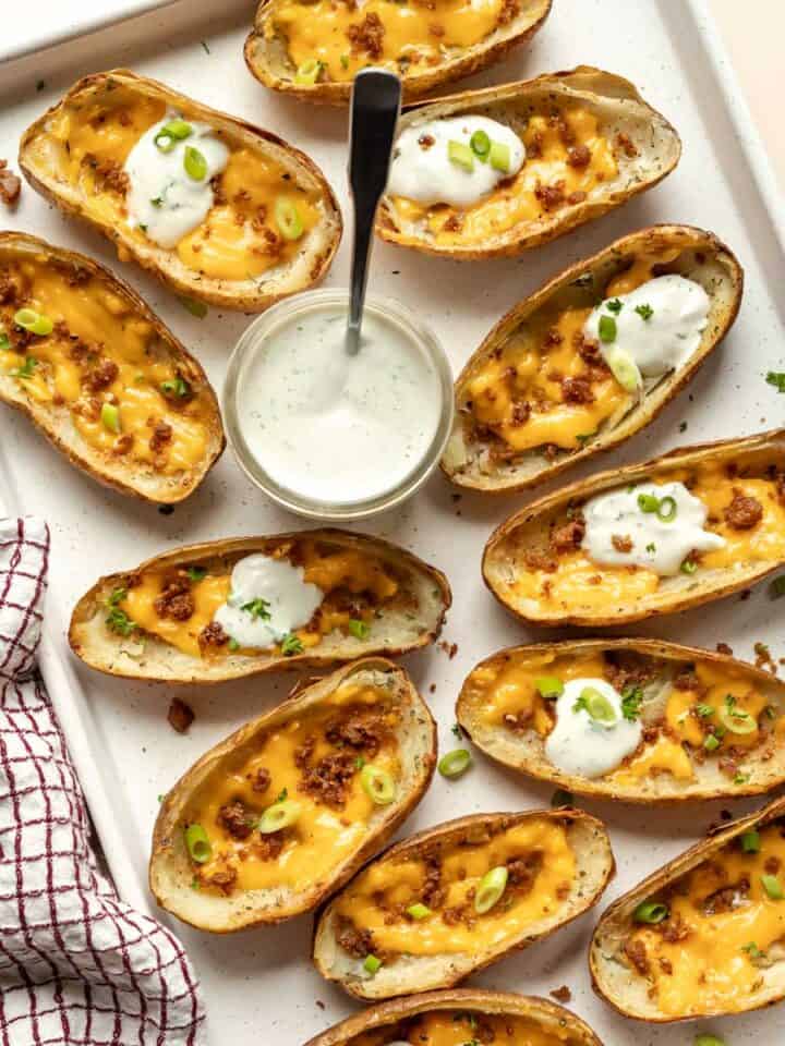 A large baking sheet filled with cheesy potato skins garnished with green onion.