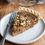 A slice of walnut pie on a small gray plate with a fork resting next to it.