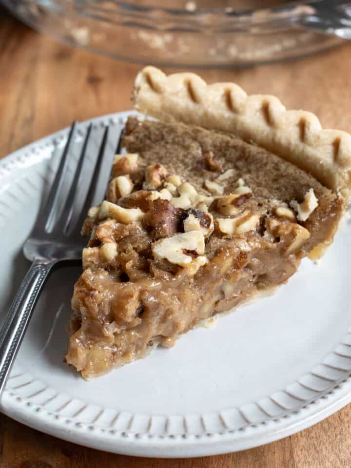 A slice of walnut pie on a small gray plate with a fork resting next to it.