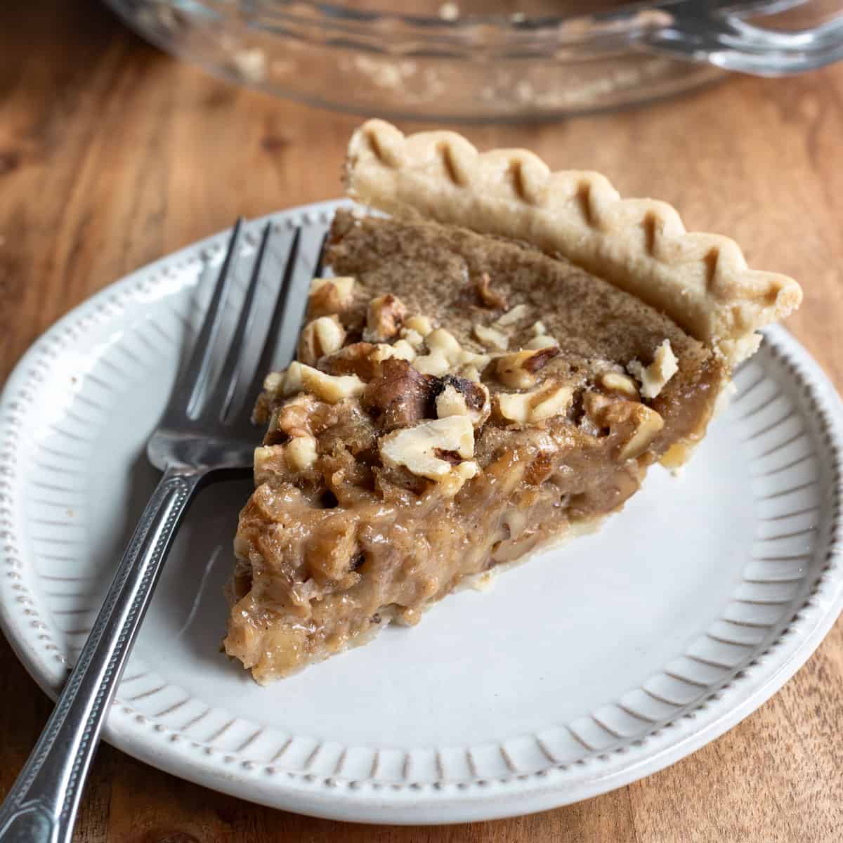 A slice of walnut pie on a small gray plate with a fork resting next to it.
