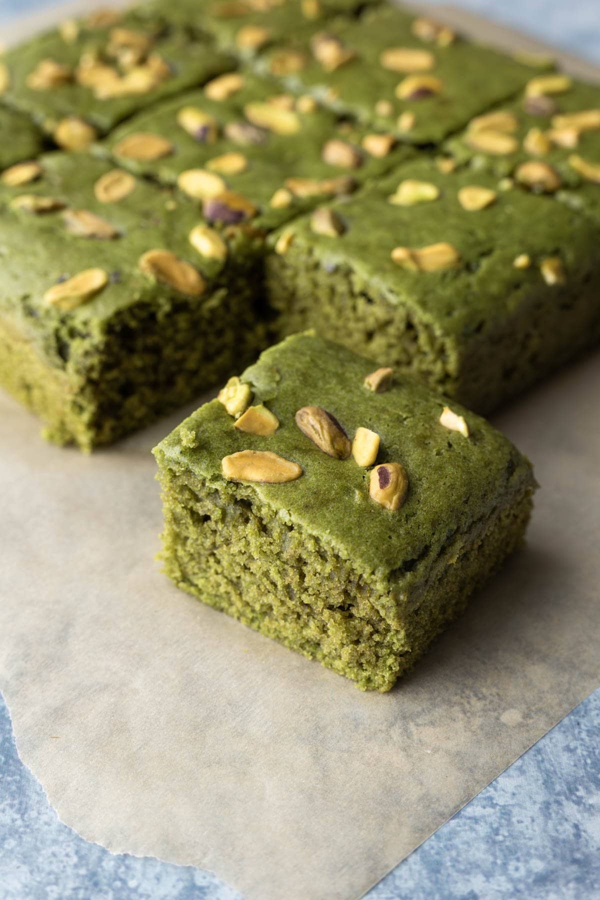 Square matcha cake with pistachios, cut into slices and resting on parchment paper.