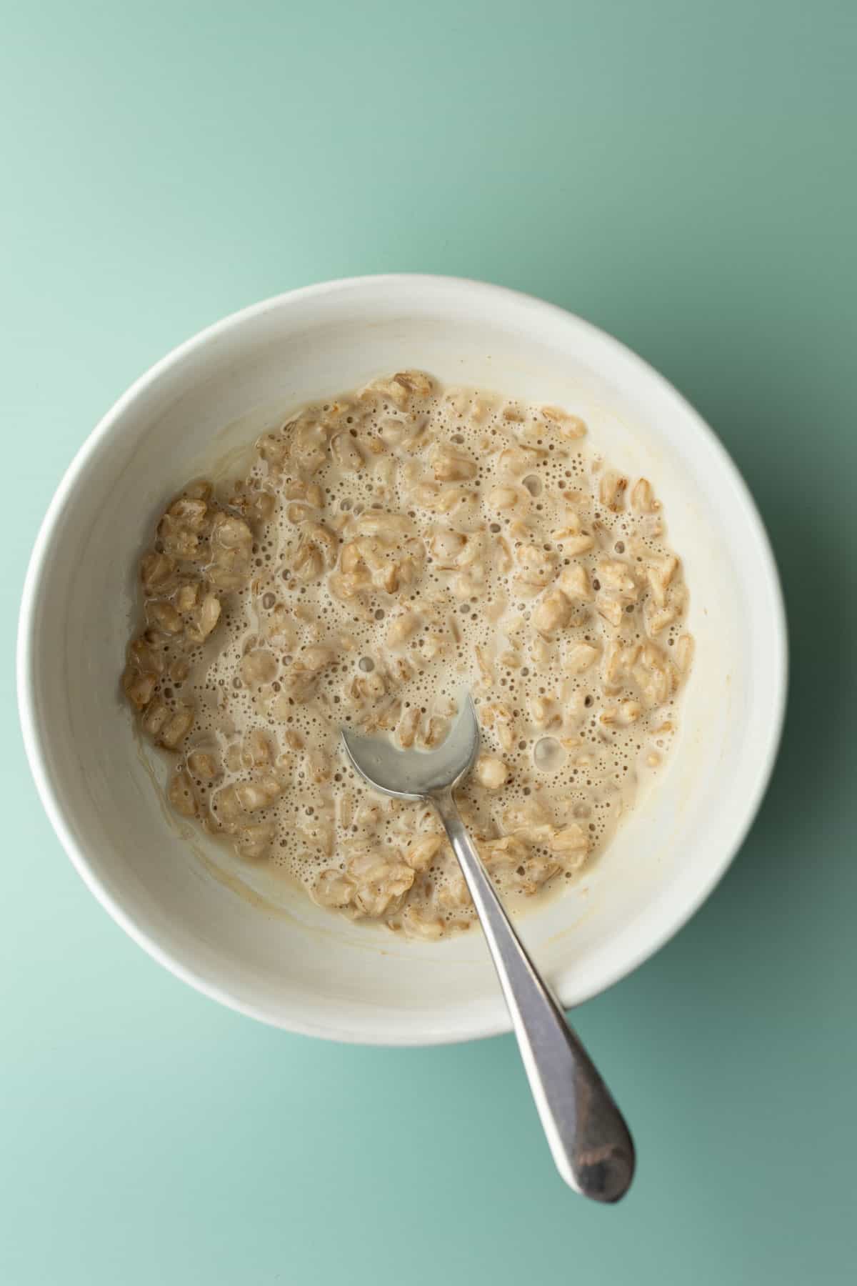 Creamy oatmeal in a white bowl, set aside to cool.