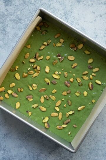 Green matcha cake batter poured into a parchment lined pan and topped with pistachios.