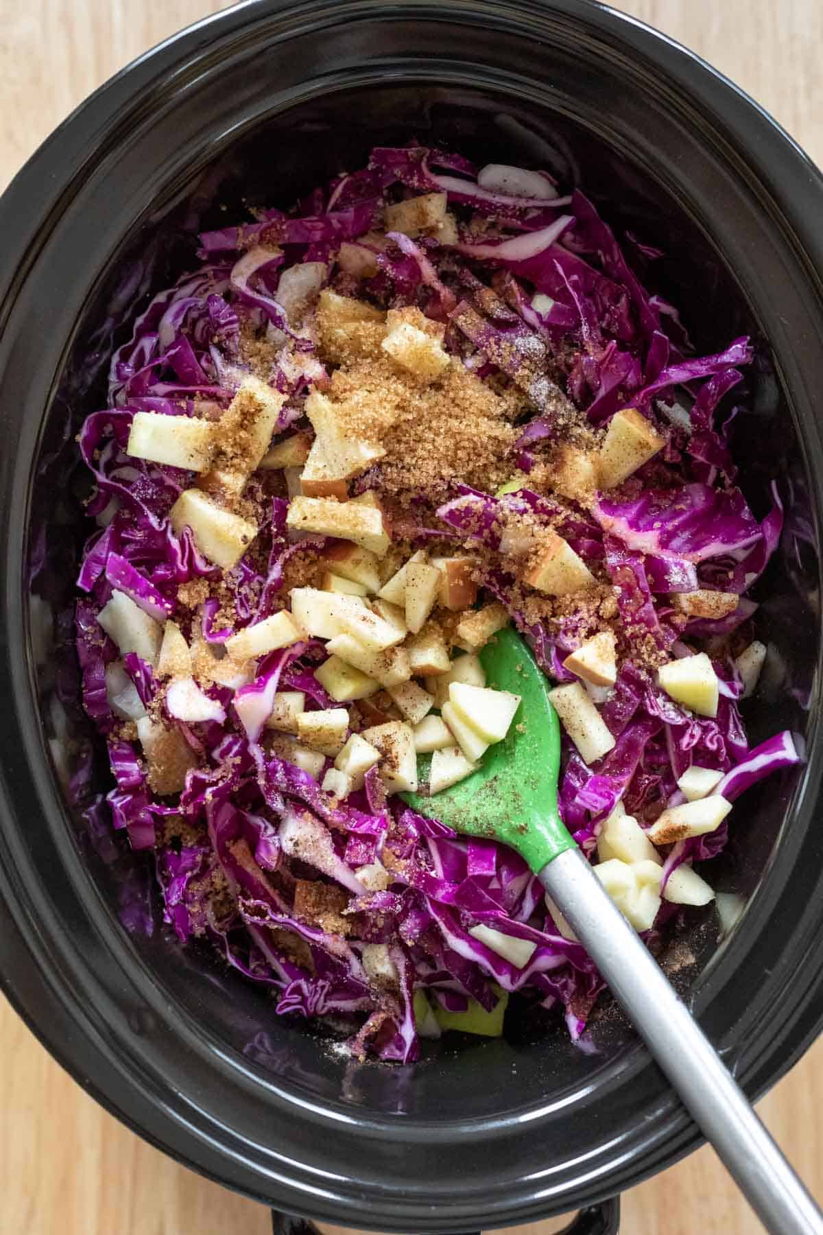 Adding chopped apples, onion, spices, and brown sugar to the red cabbage in the slow cooker.