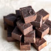 Squares of dark chocolate fudge stacked up on top of parchment paper.