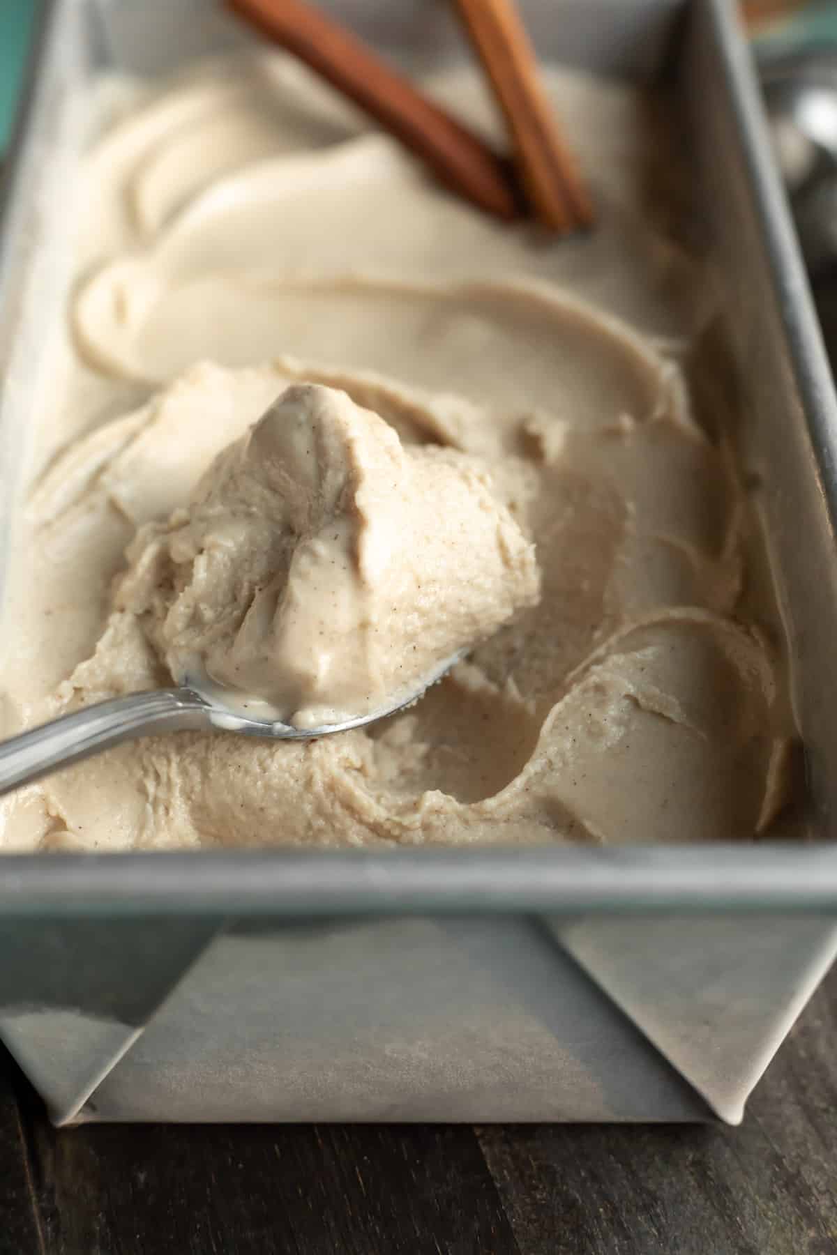 A spoon scooping up creamy vegan ice cream from a metal loaf pan.