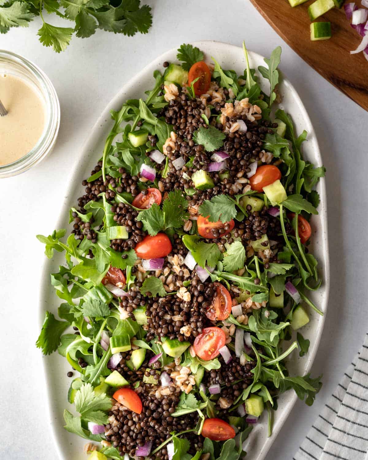 Arugula salad on a serving platter topped with black lentils, tomatoes, red onion, and farro.