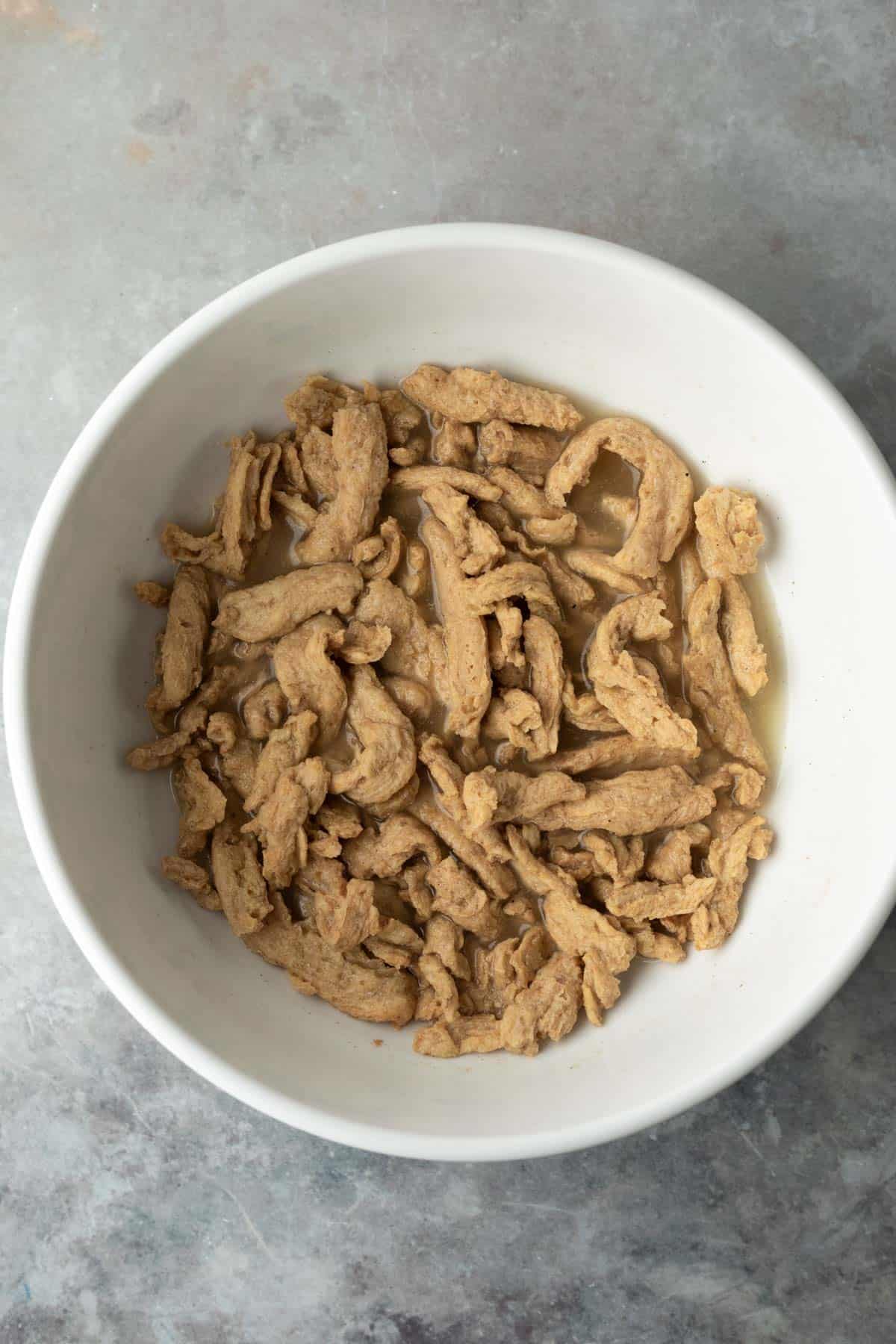 overhead of soy curls soaking in a white bowl.