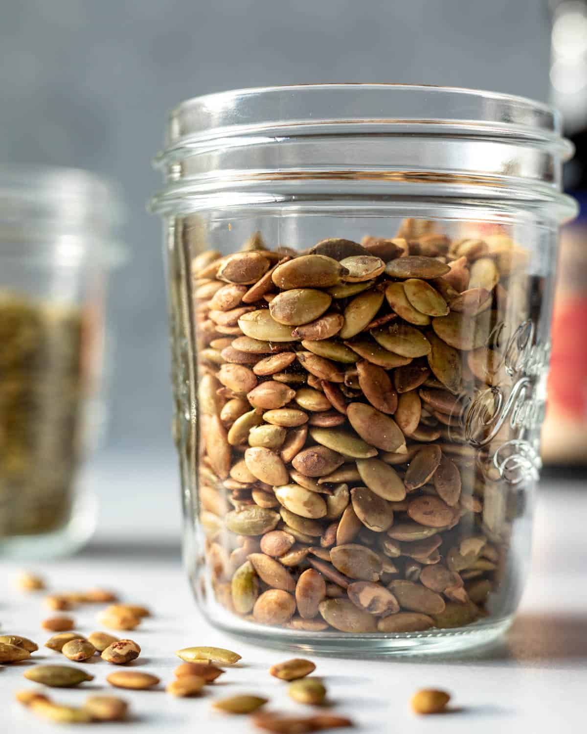 A glass jar filled with toasted tamari pumpkin seeds for sprinkling on salads.