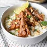 Slices of baked tempeh in peanut sauce resting on rice in a white bowl.