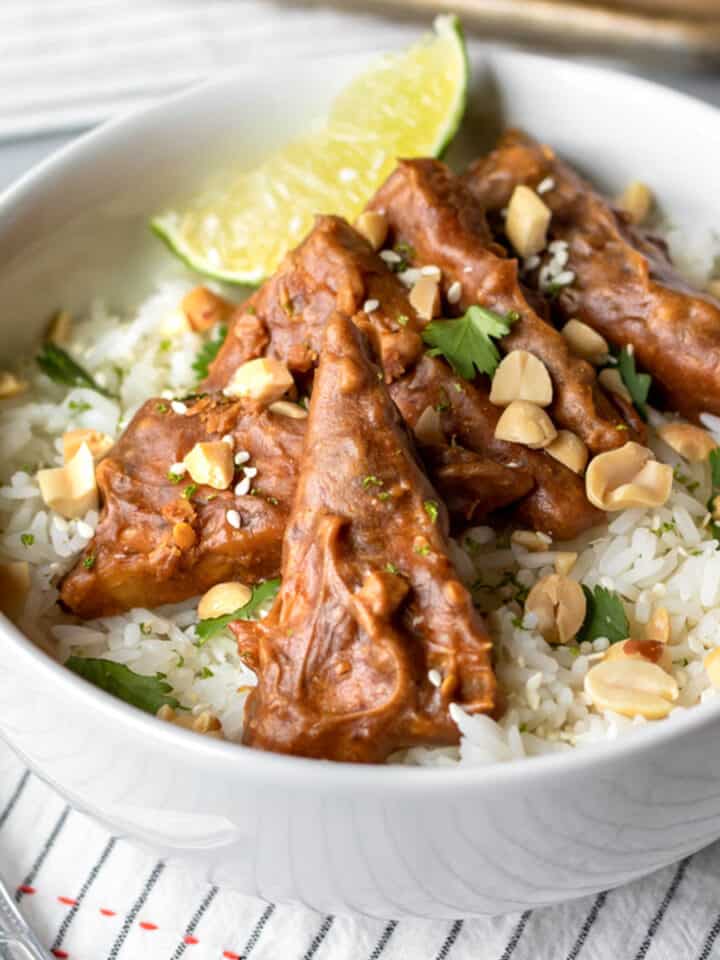 Slices of baked tempeh in peanut sauce resting on rice in a white bowl.