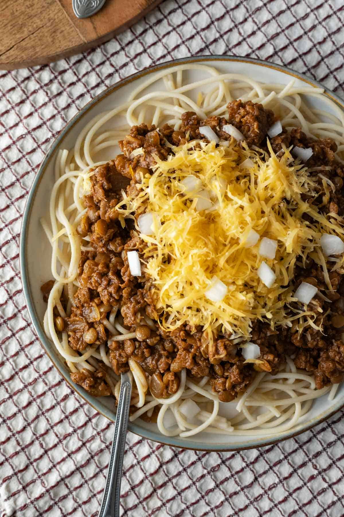 Serving of vegan Cincinnati chili over spaghetti topped with cheddar and onion.