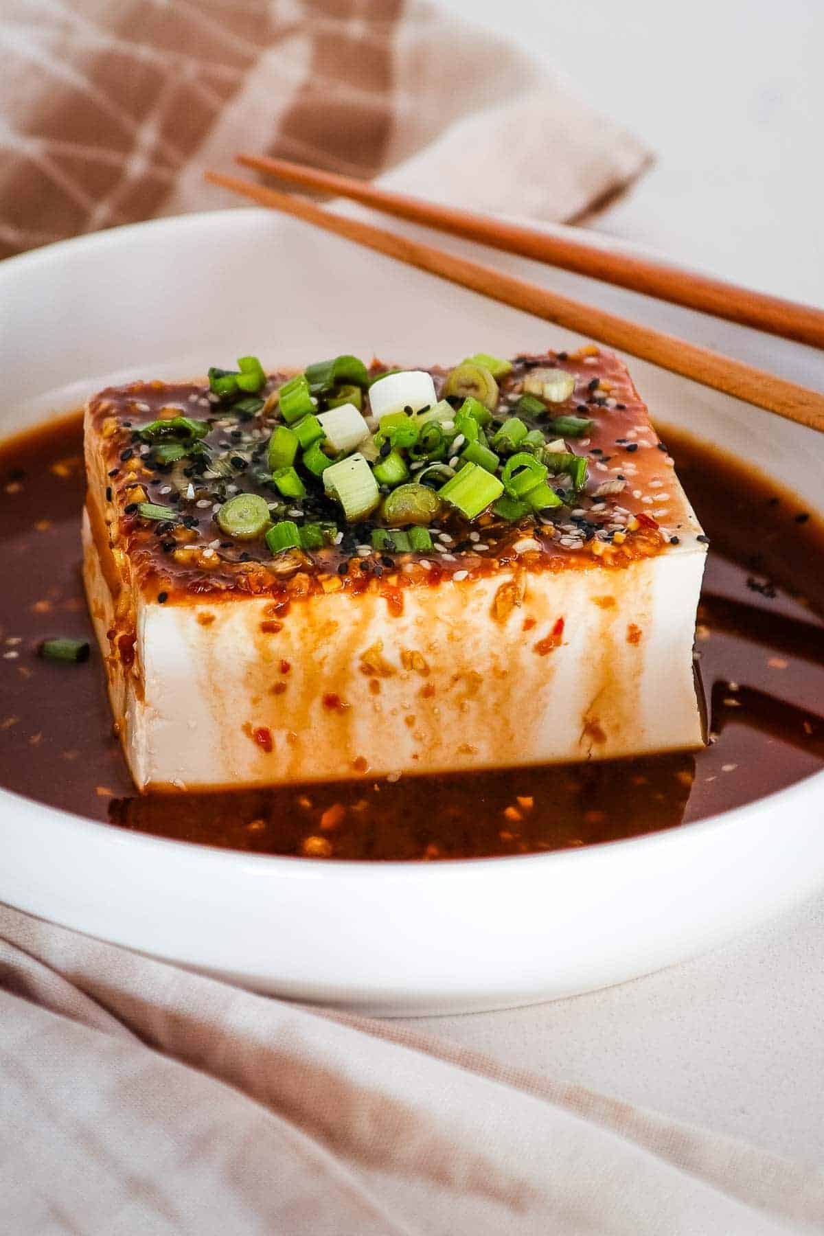 silken tofu with spicy soy dressing over top and garnished with green onions and sesame seeds.