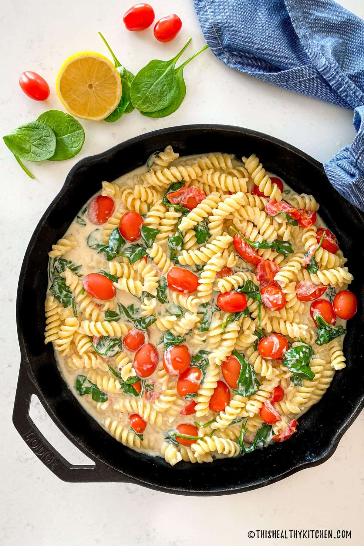 rotini pasta with spinach, tomatoes, and tofu pasta sauce in a skillet.