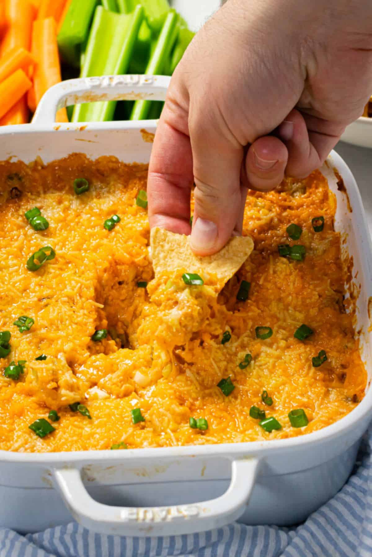 scooping dip out of a casserole dish with a tortilla chip.