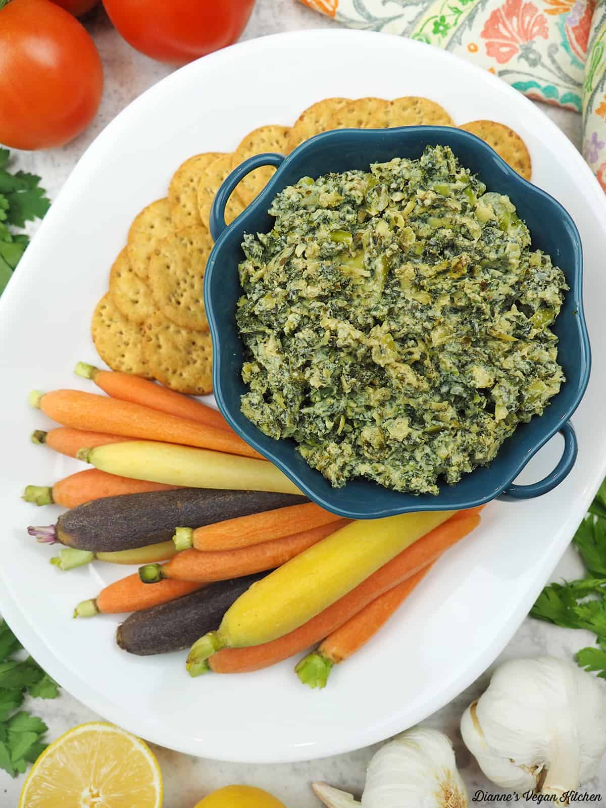 spinach artichoke dip on a platter with carrots and crackers.
