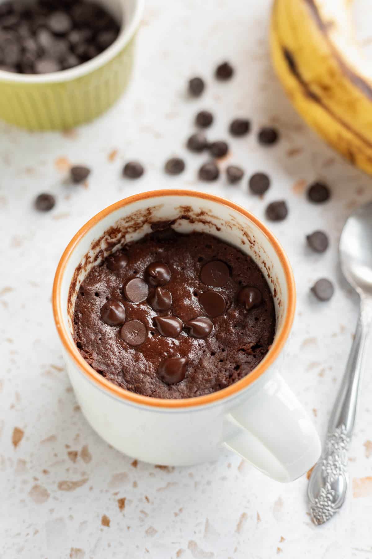 A microwaved brownie with chocolate chips on top in a small white mug.
