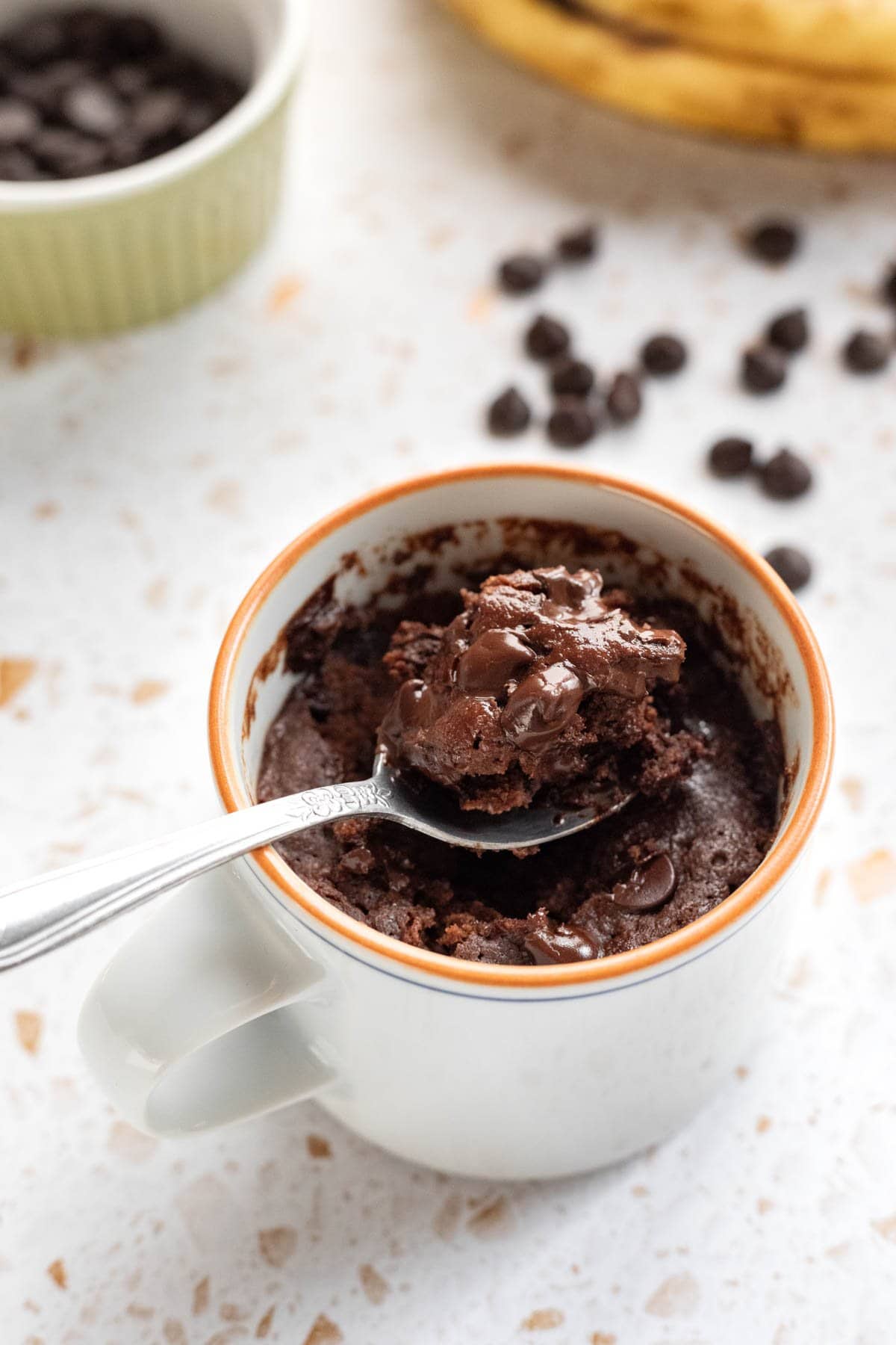 A spoon scooping up a bite of healthy brownie from a white mug.