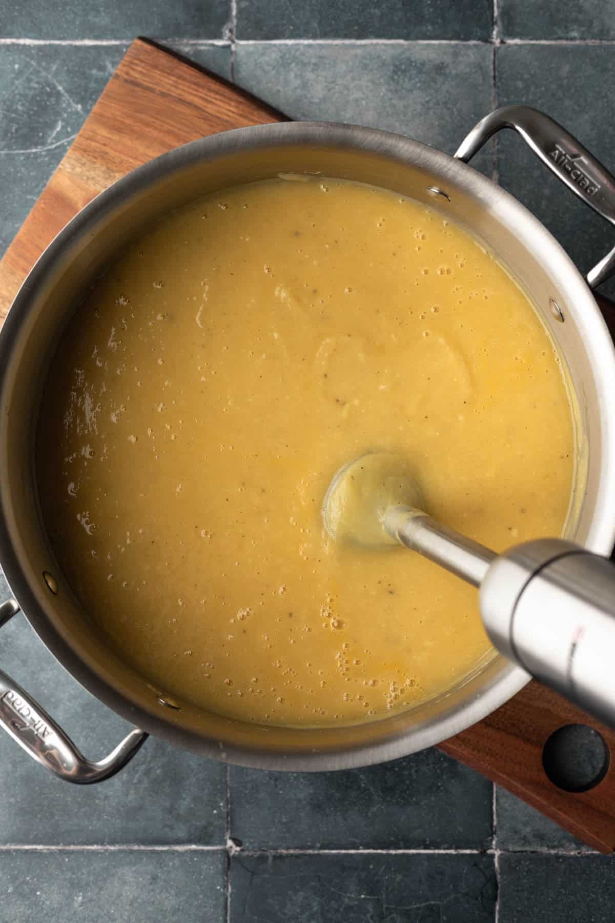 Using an immersion blender to puree the creamy soup.