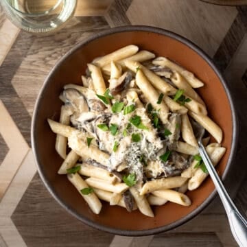 overhead of bowl of shiitake mushroom pasta with vegan parmesan and fresh herbs.