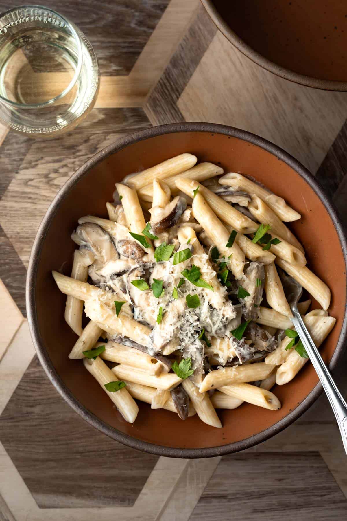 Shiitake mushroom pasta in a bowl with a fork and glass of white wine nearby.