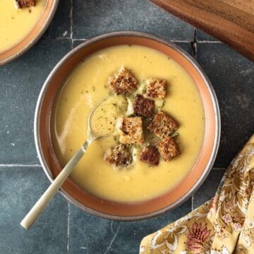 A bowl filled with creamy white sweet potato soup garnished with croutons and resting on a dark tile countertop.