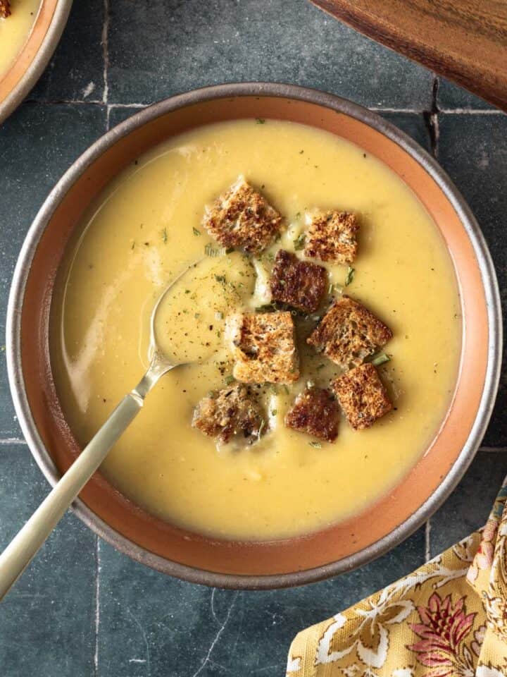 A bowl filled with creamy white sweet potato soup garnished with croutons and resting on a dark tile countertop.