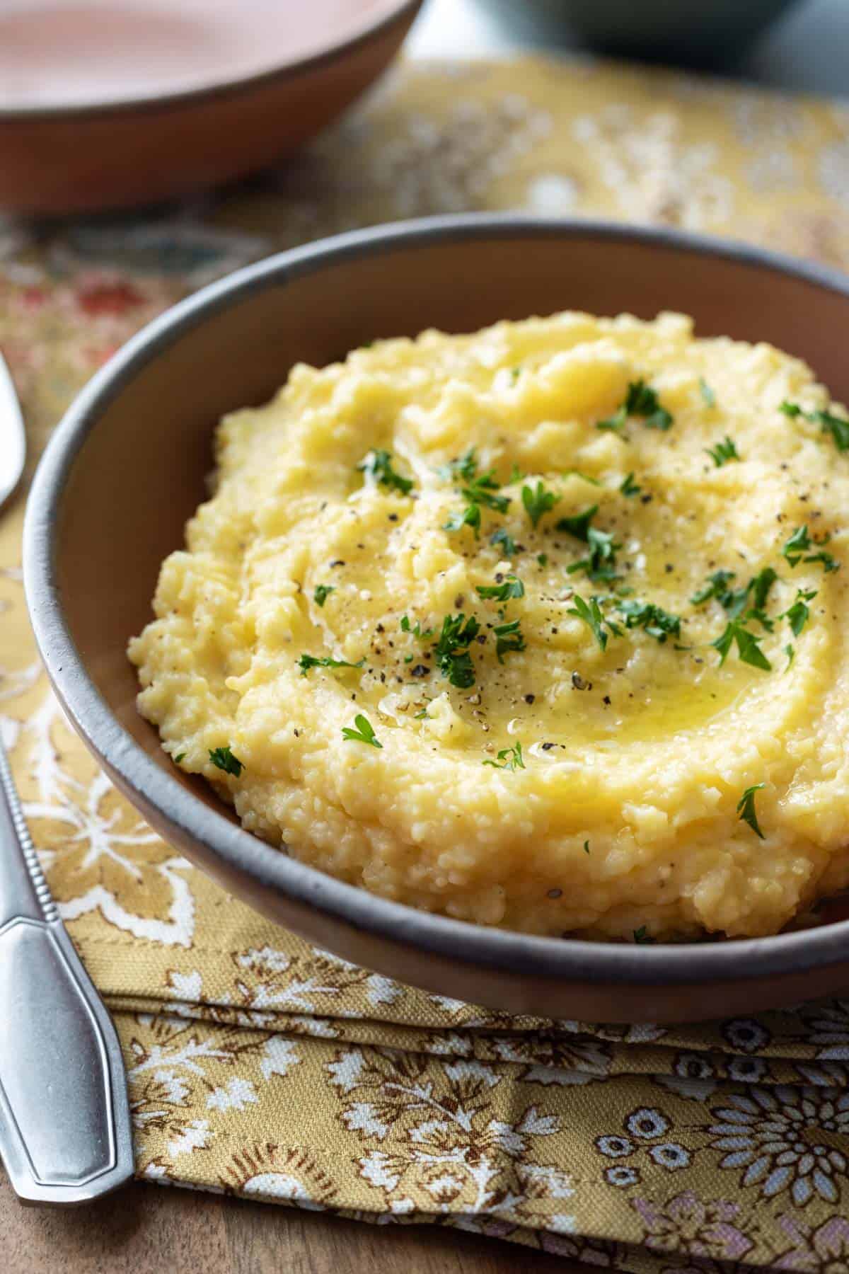 Polenta garnished with olive oil and parsley in a red serving bowl.