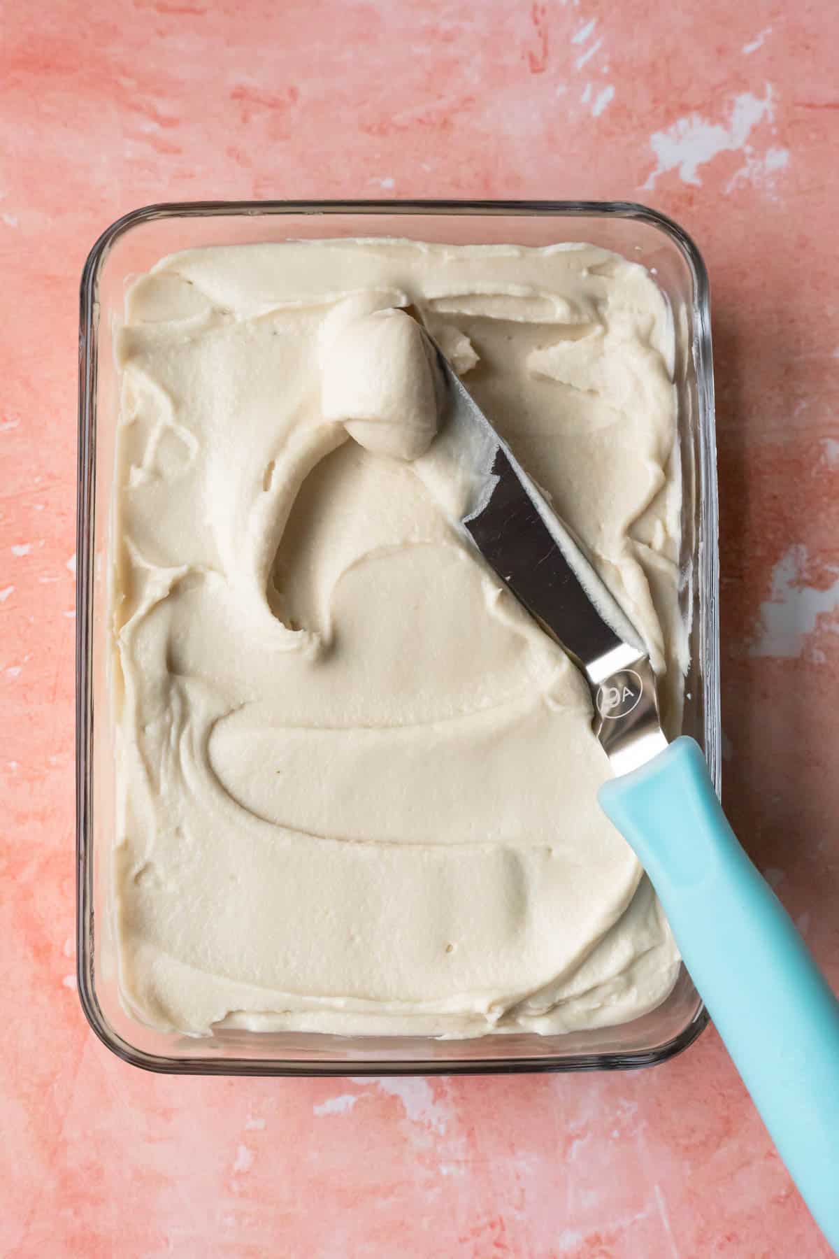 An offset spatula spreading the almond flour frosting in a glass dish to chill.