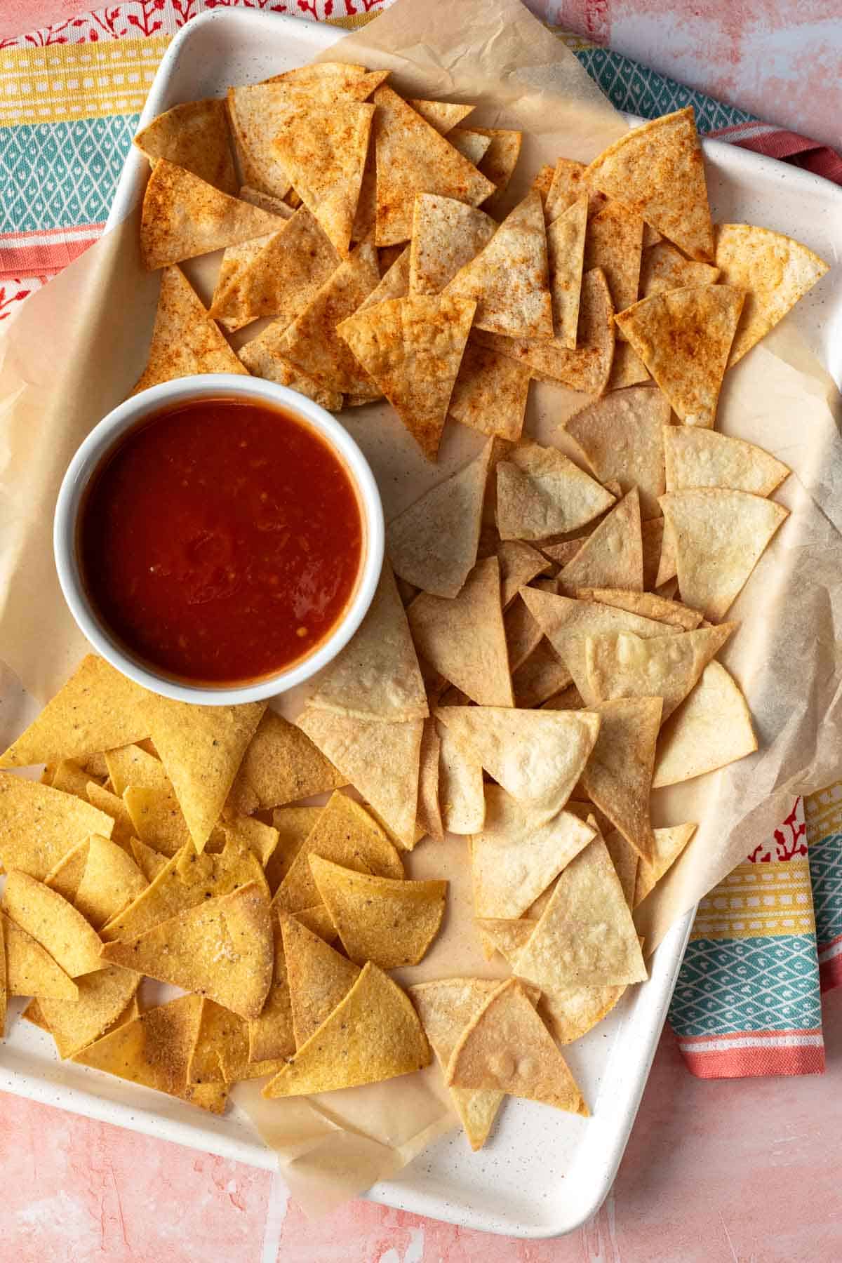 overhead shot of air fryer tortilla chips on a baking sheet with a cup of salsa.