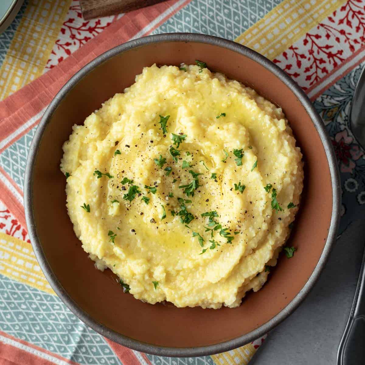 A red bowl filled with vegan polenta with parsley and black pepper on top.
