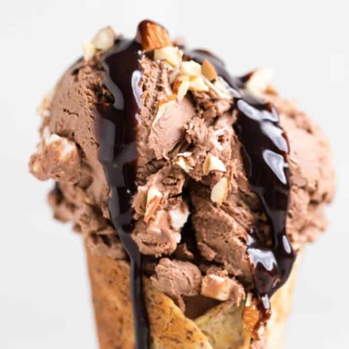 close-up shot of vegan rocky road ice cream in a cone with chocolate syrup.