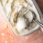 An ice cream scoop resting in a pan of coconut ice cream sprinkled with toasted coconut.