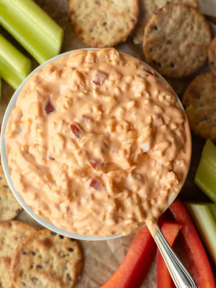 Overhead view of dairy free pimento cheese dip in a bowl surrounded by veggies and crackers.