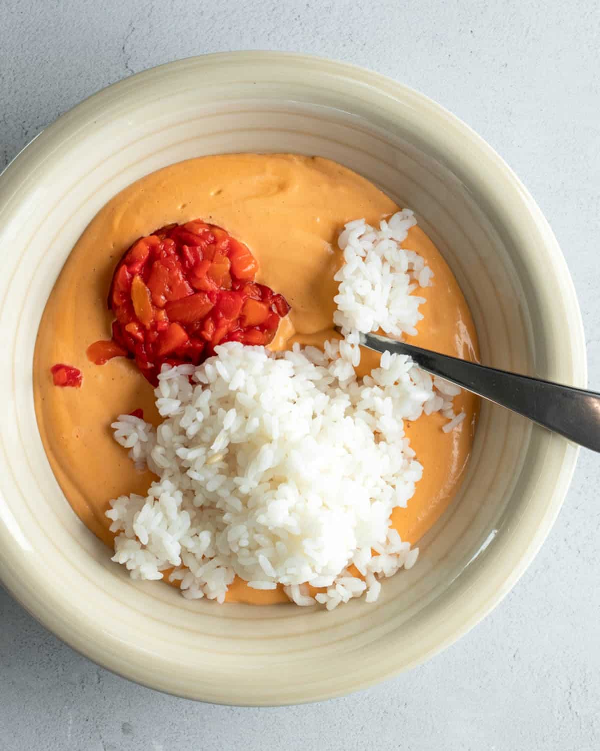 The blended pimento cashew sauce in a bowl with the rice and diced pimentos.