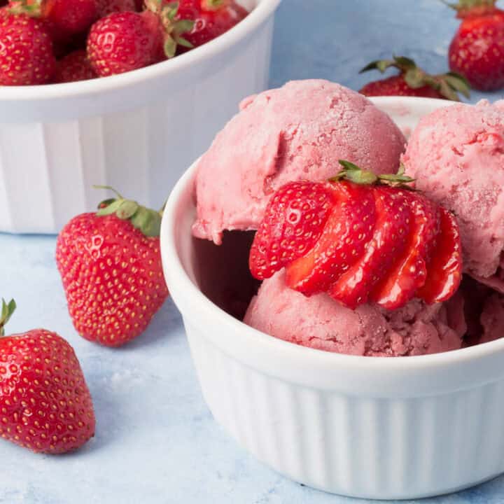 vegan strawberry ice cream in a white bowl with strawberries.