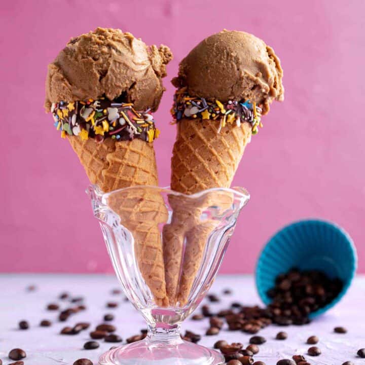 two sugar cones with vegan coffee ice cream standing in a glass sundae dish.