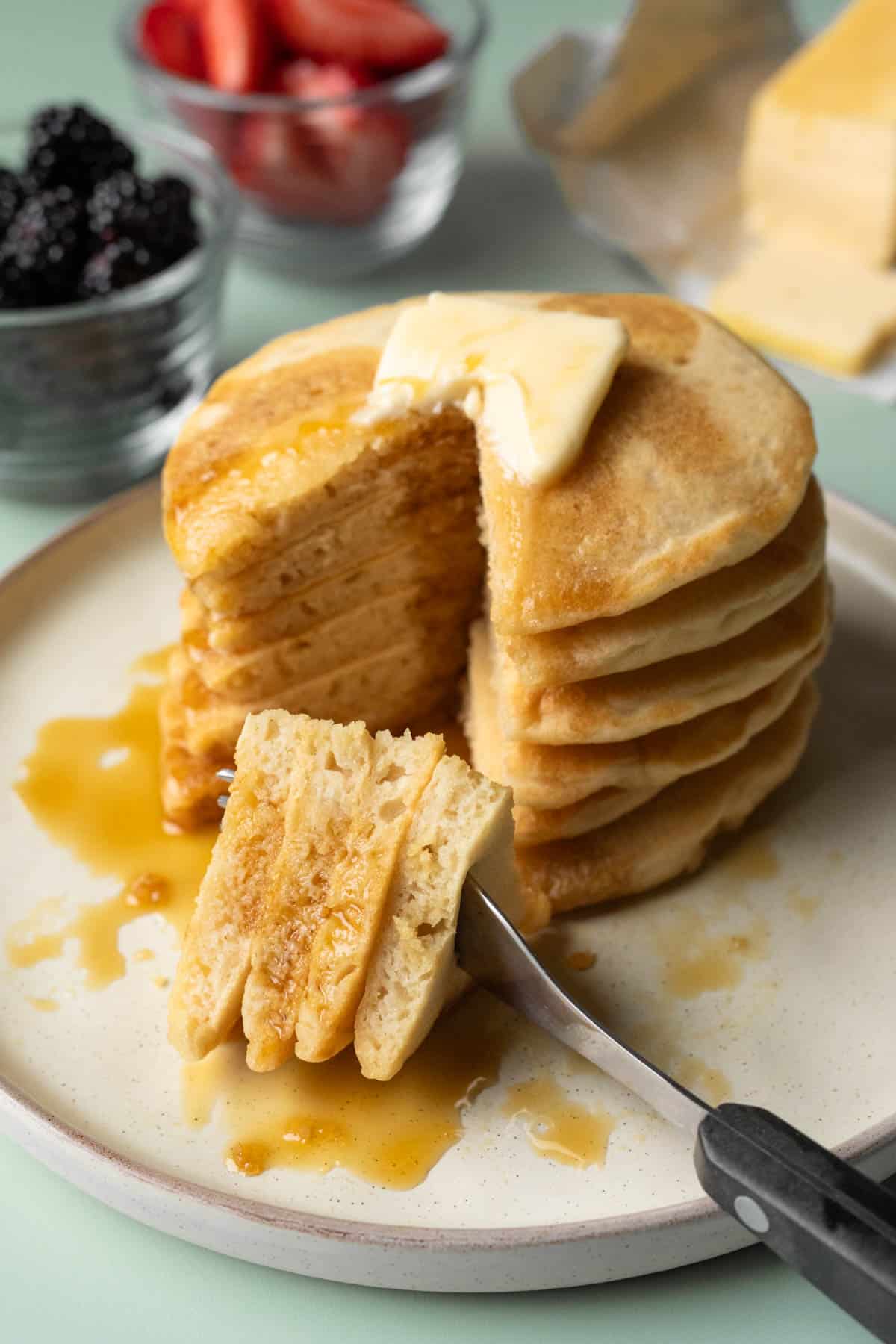 Stack of vegan pancakes on a plate with a piece taken out by a fork.
