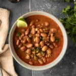 A bowl filled with rich vegan charro beans in broth against a dark background.