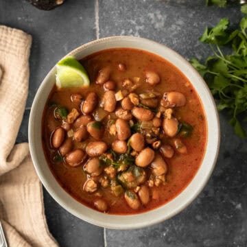 A bowl filled with rich vegan charro beans in broth against a dark background.