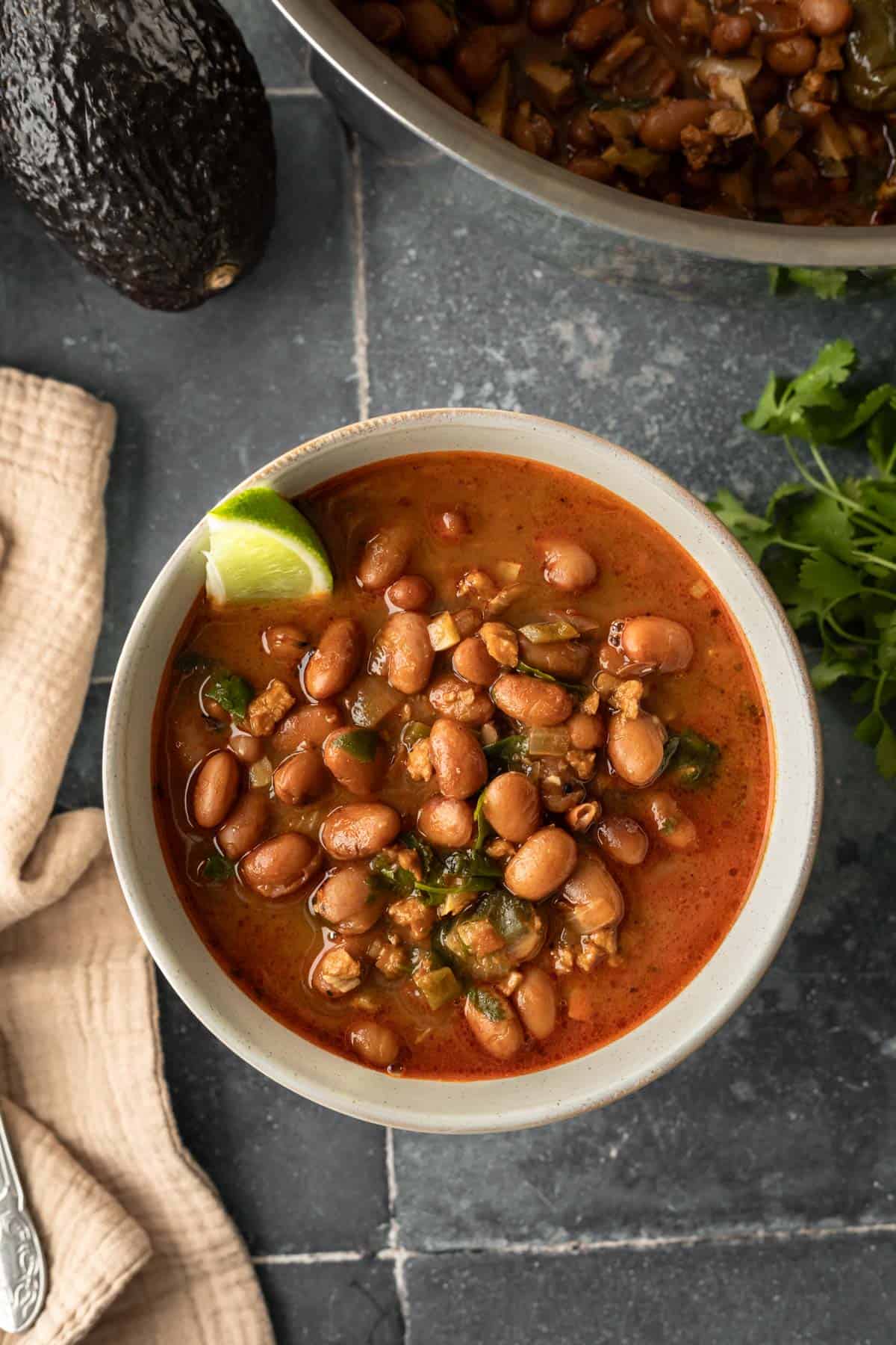 Bowl of vegan beans with spoon and napkin and avocado nearby.