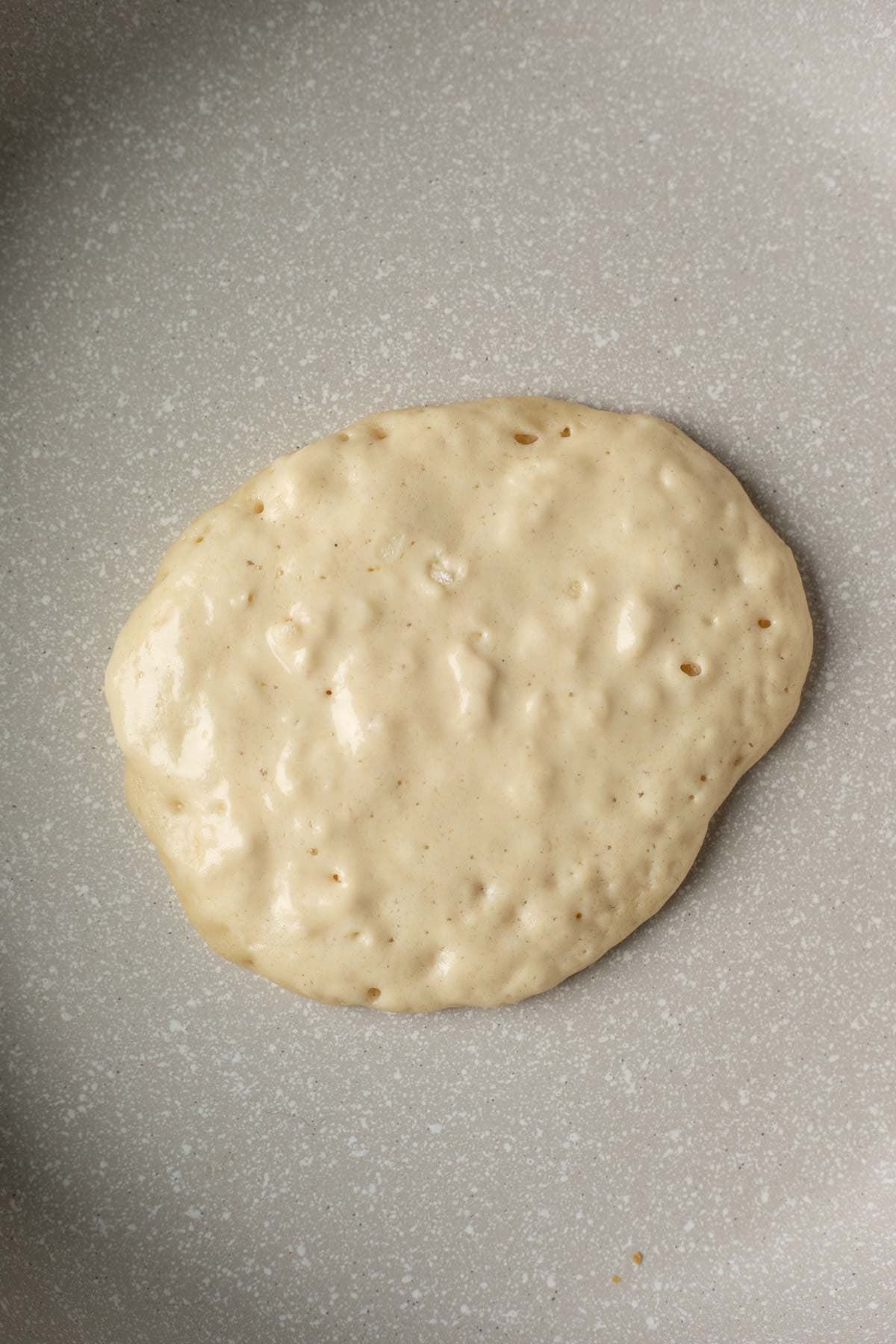 A vegan pancake with edges setting and bubbles forming on top.