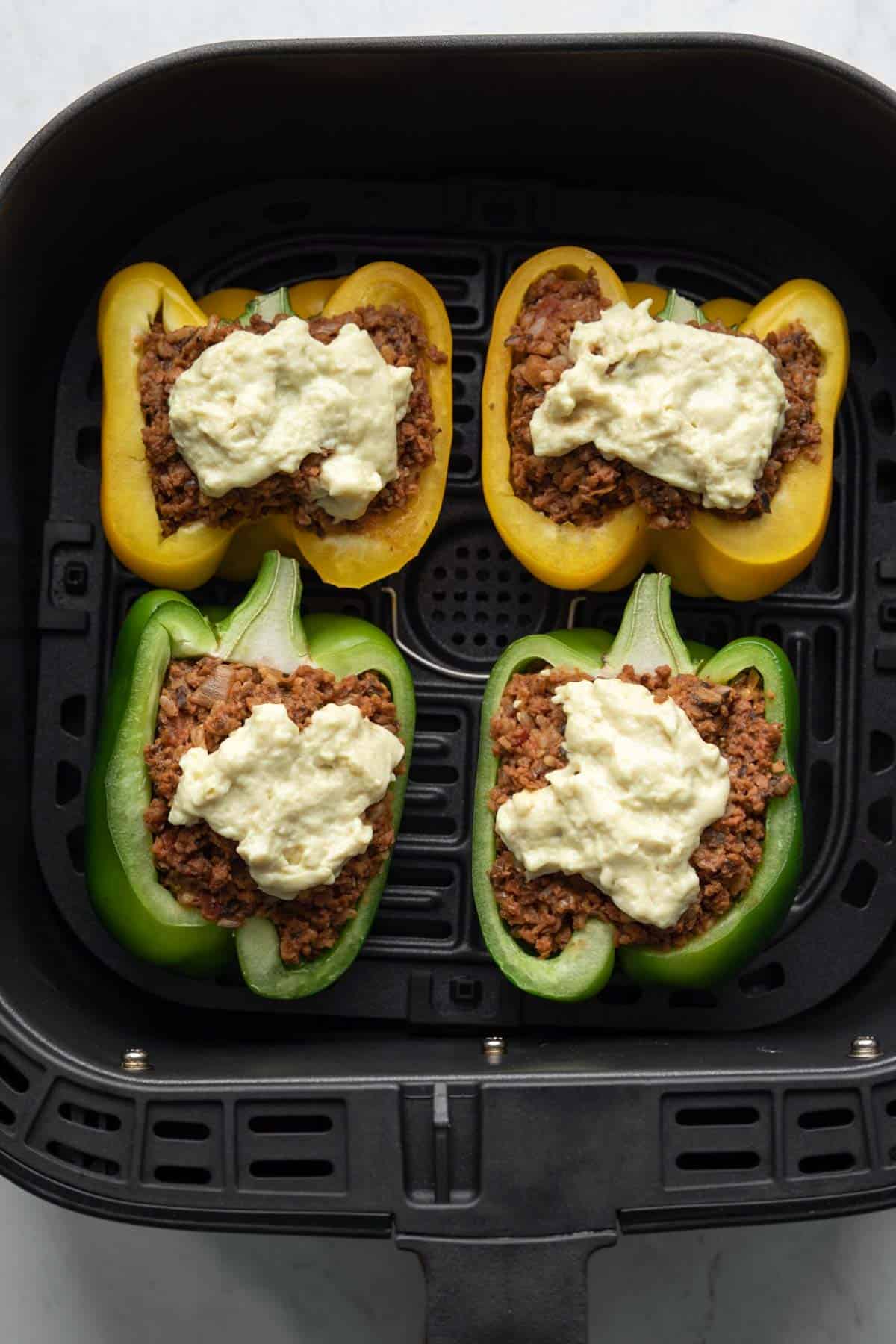 Four stuffed peppers in an air fryer basket.
