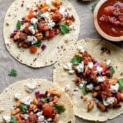 Three bean tacos on a sheet pan sprinkled with cheese and toppings.