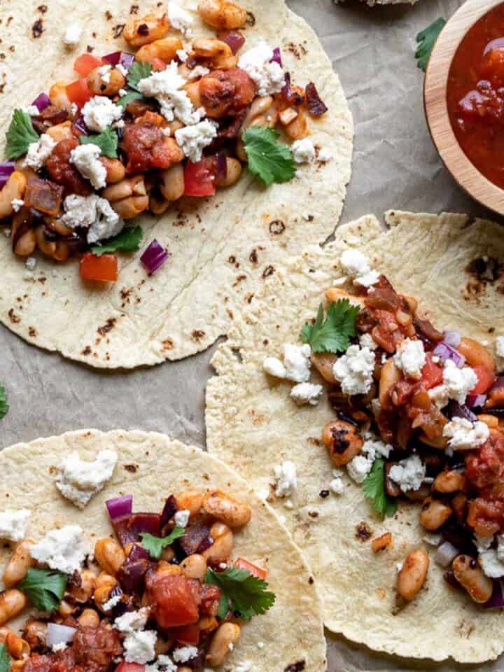 Three bean tacos on a sheet pan sprinkled with cheese and toppings.
