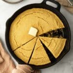 Close-up overhead view of southern vegan cornbread in a cast iron skillet with a piece missing.